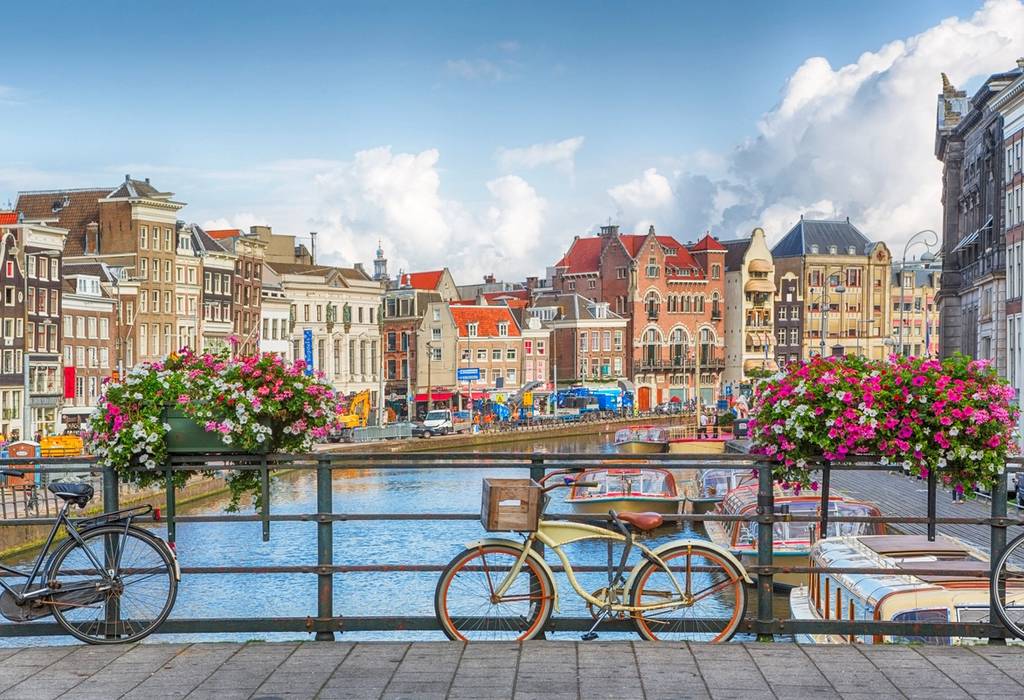 View of a canal in Amsterdam with a bike attached to a guard rail topped with pink and white flowers