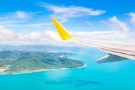 A view of the wing of a plane flying over a tropical destination