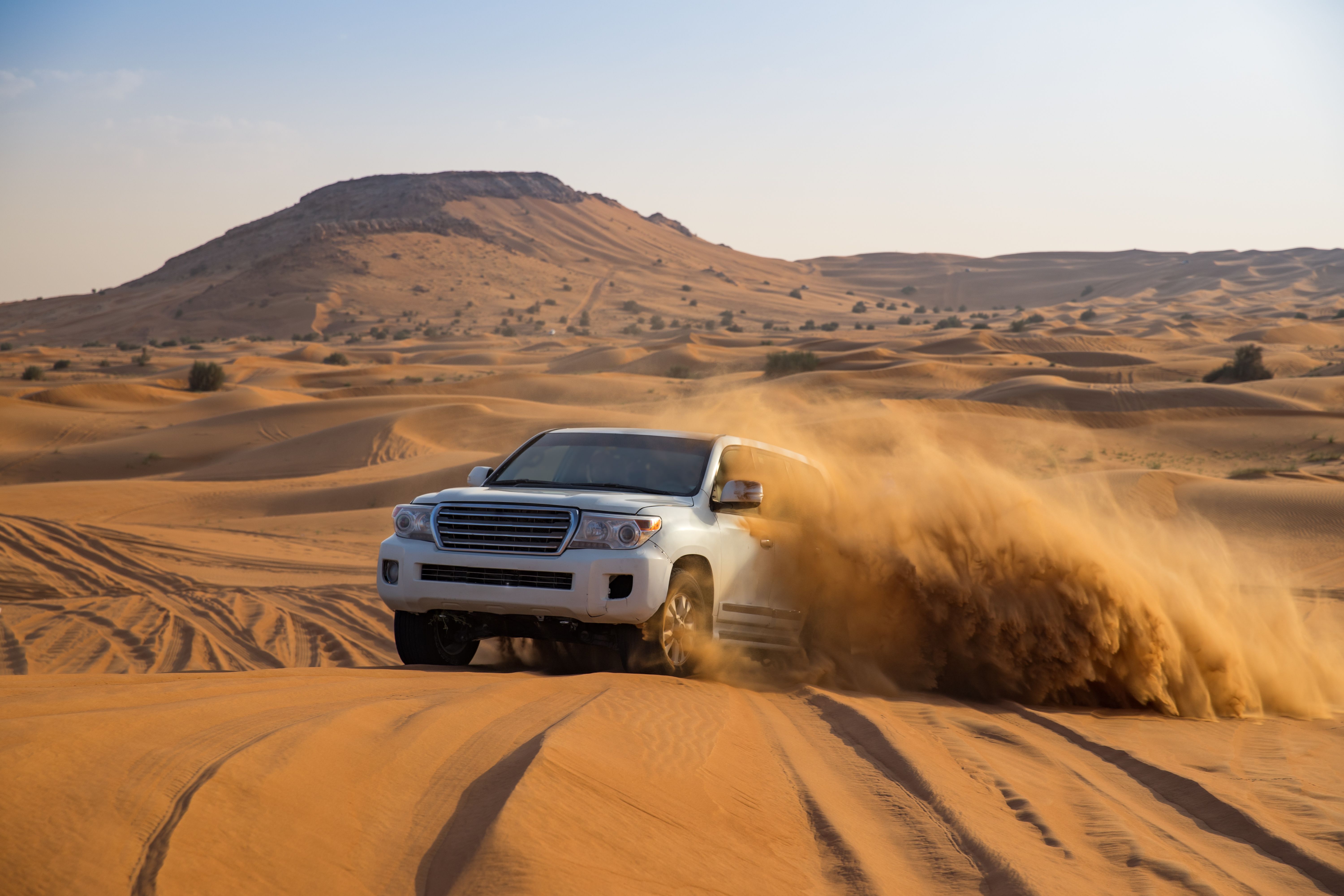 A 4x4 jeep driving through golden sand dunes in Dubai, kicking up sand sprays as it goes