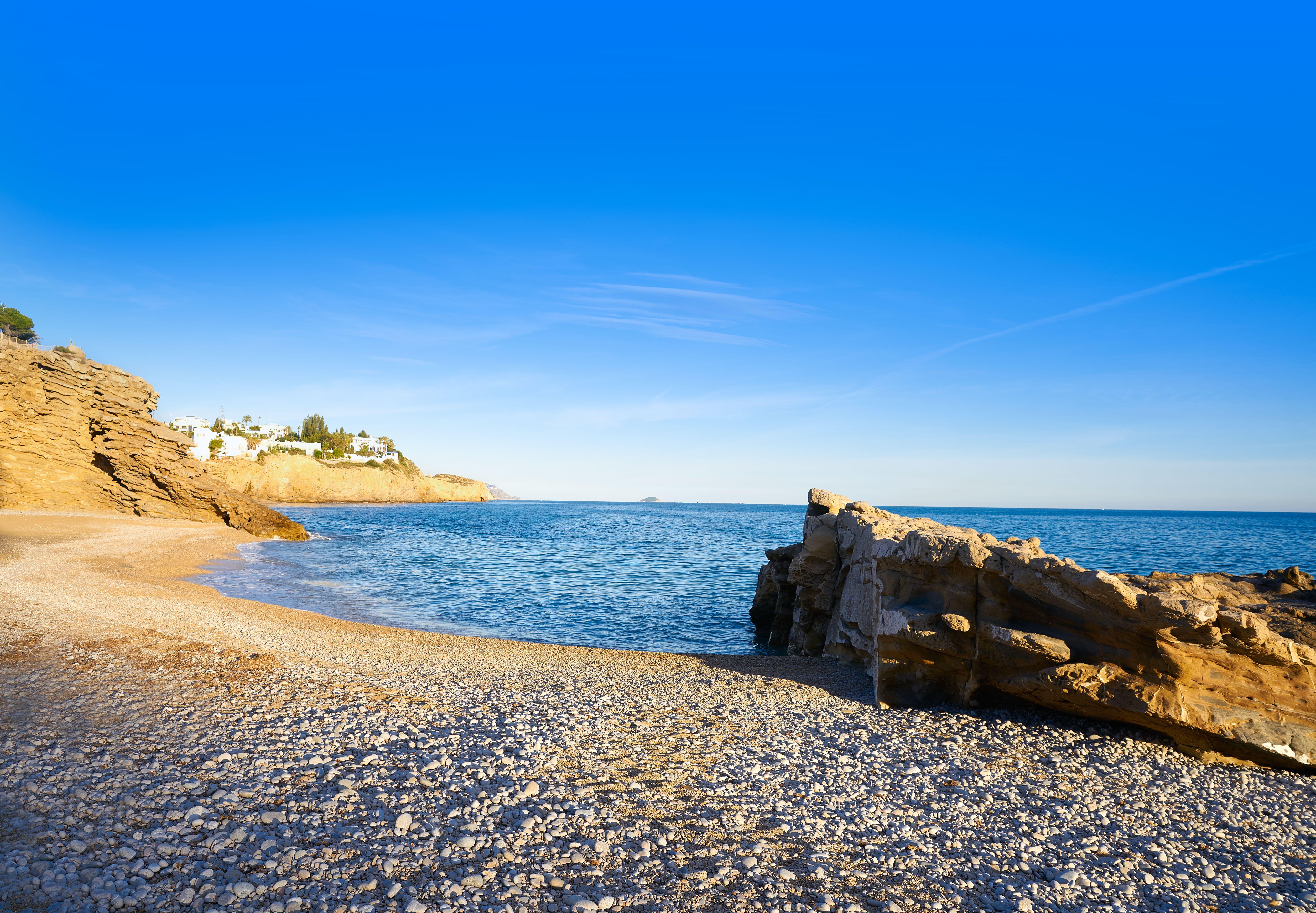 A golden sand-and-pebble cove in soft, early-morning light