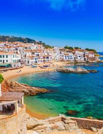 A view of whitewashed buildings and golden sandy beach in the town of Calella de Palafrugell on a sunny day