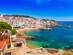 A view of whitewashed buildings and golden sandy beach in the town of Calella de Palafrugell on a sunny day