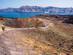 Hikers walking along the narrow dirt paths across a volcanic landscape in Santorini with cruise ships moored in the sea in the background