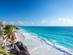 Wide-angle view of the frothy turquoise waters of the Caribbean Sea, a small white-sand beach with a palm tree and the ruins of Tulum, Mexico
