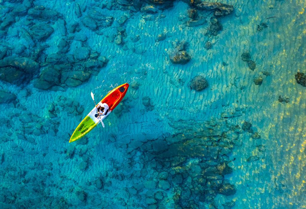 Aerial view of a women in a green, white and red kayak in incredibly clear seas