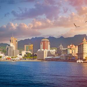 A view across the sea of Port Louis town in Mauritius as the sun sets with mountains in the background