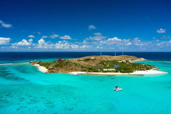 An aerial view of a catamaran in the sea and a small island fringed with white sands and surrounded by textbook Caribbean turquoise waters