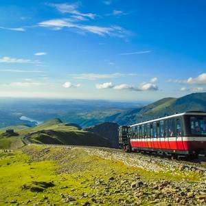 View of a red train on its way up Mount Snowdon with far-reaching views of the mountain and valley below