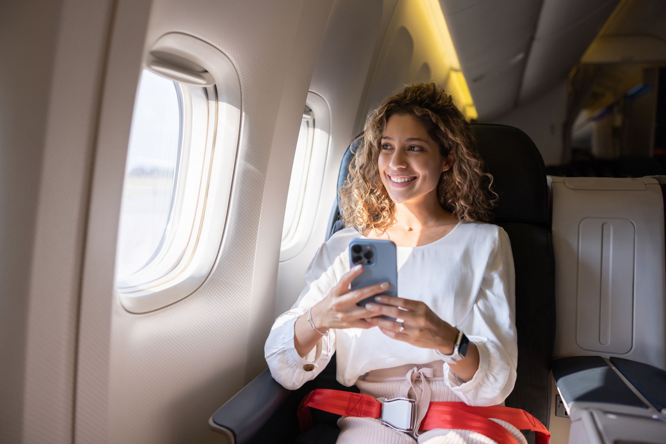 Female traveller using her phone on an airplane and looking through the window