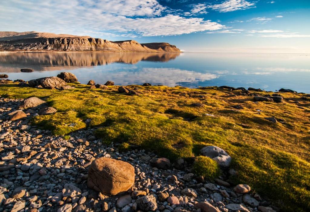 A view looking out across a bay in the Westfjords in Iceland on a bright crisp day with clear water reflecting the sky