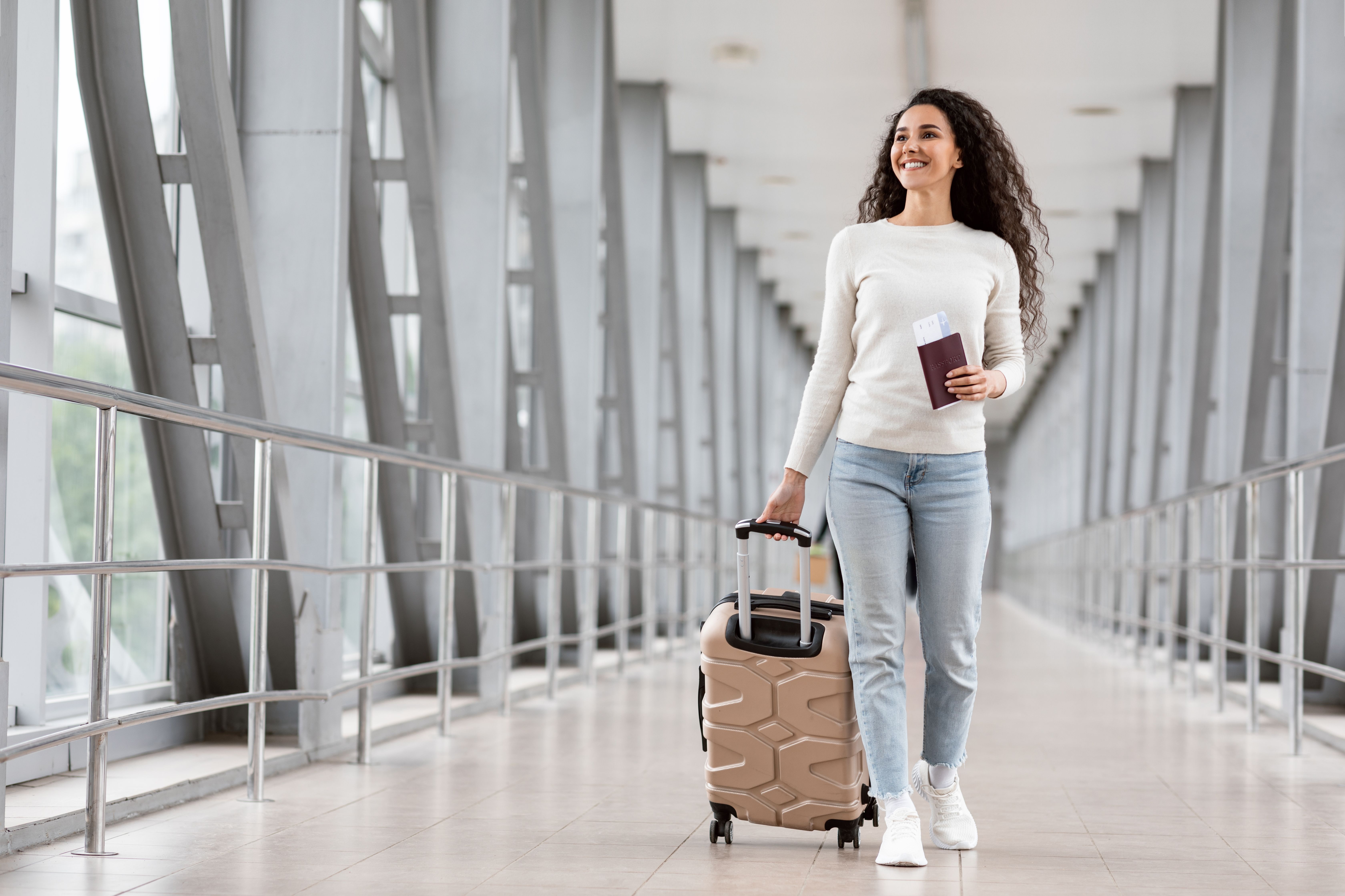 A woman walking through an airport with a small suitcase, holding her passport