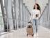 A woman walking through an airport with a small suitcase, holding her passport