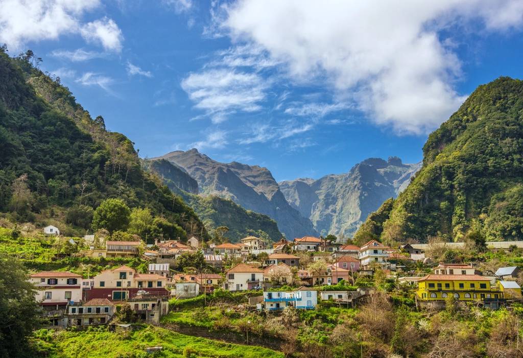 A view on traditional beige and yellow houses nestles among towering green mountains