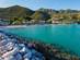 View across calm turquoise water toward a sun-lounger lined beach hemmed in by tree-covered mountains