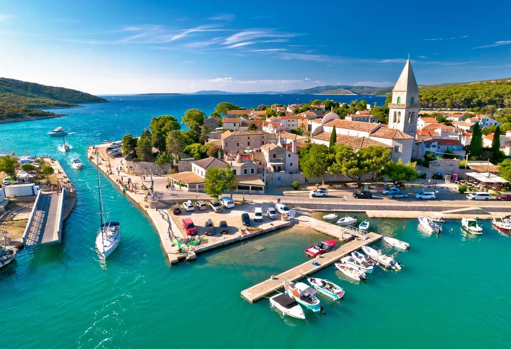 Aerial view of boats sailing through a narrow channel between two islands in Croatia, with Osor town on the right