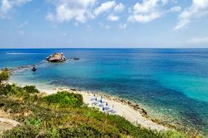 A view of clear blue water and sandy beach with sunbeds and umbrellas near Aphrodite bath in Polis, Cyprus