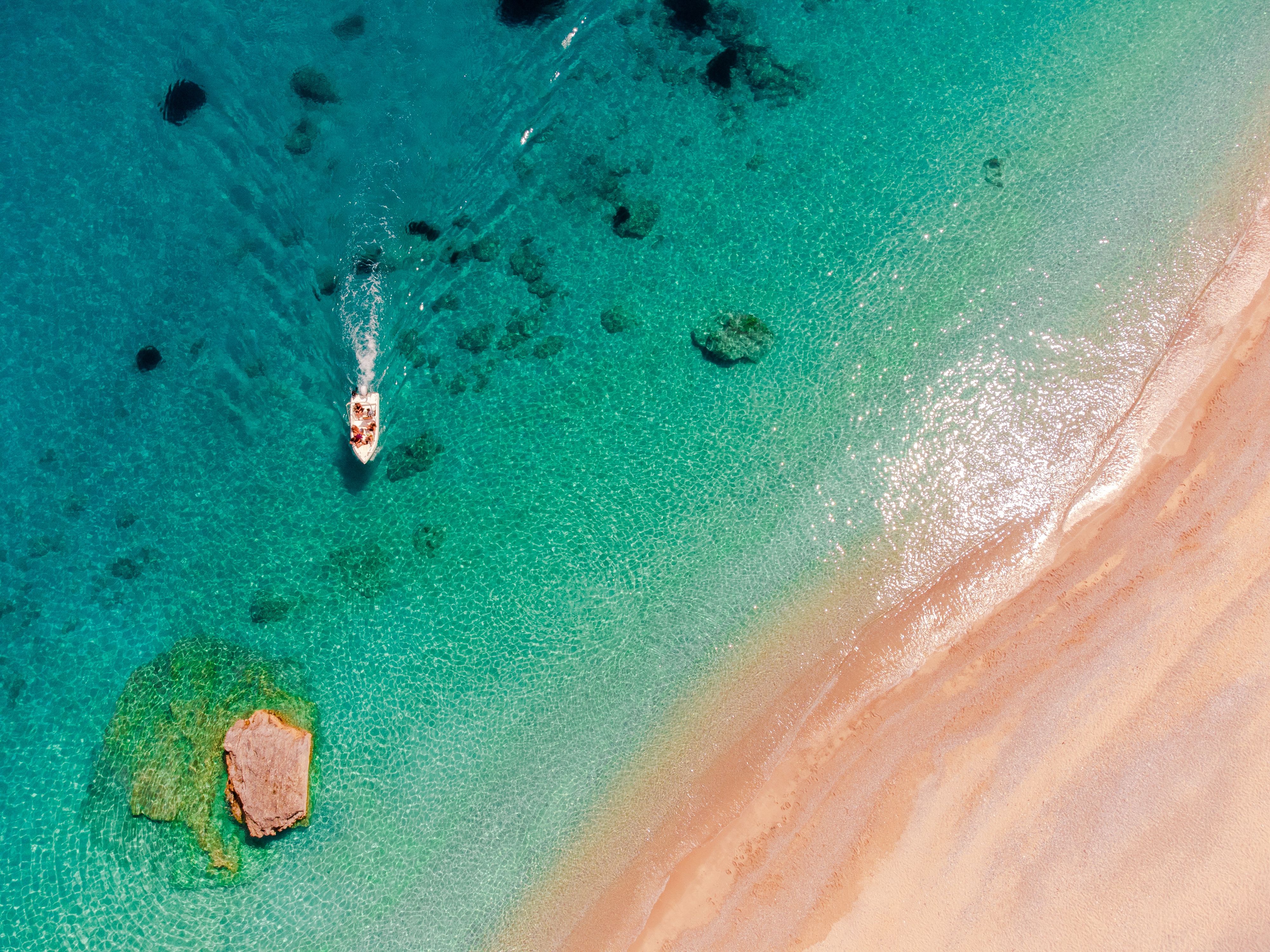 Bird's eye view of a small boat sailing on the blue-green waters of an empty beach in Corfu