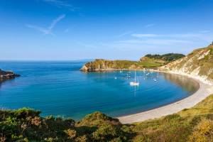 A view of the curved, sandy beach at Lulworth Cove with boats anchored in the calm sea