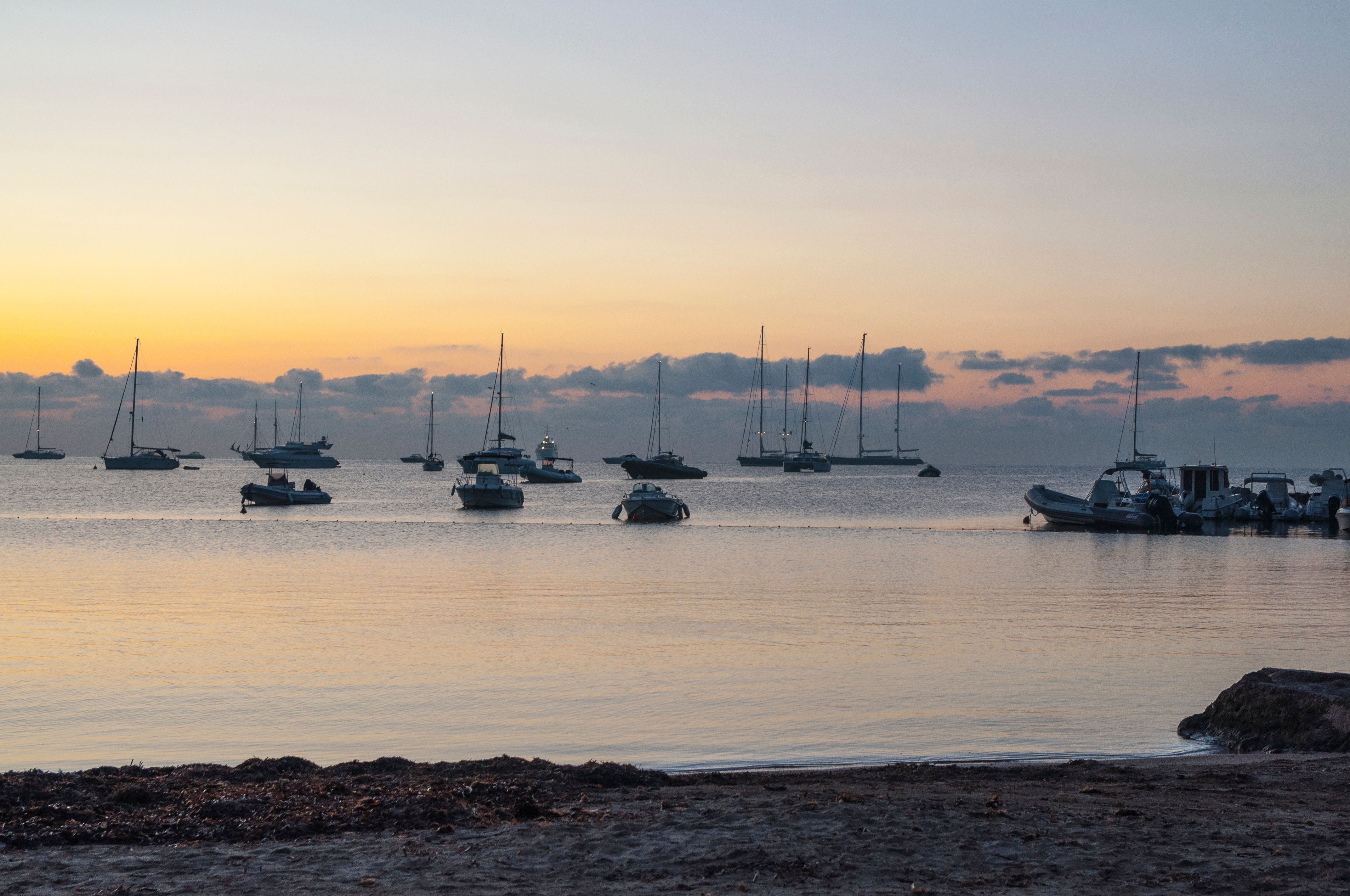 View of yachts bobbing in calm bay waters in the soft, pre-sunrise glow