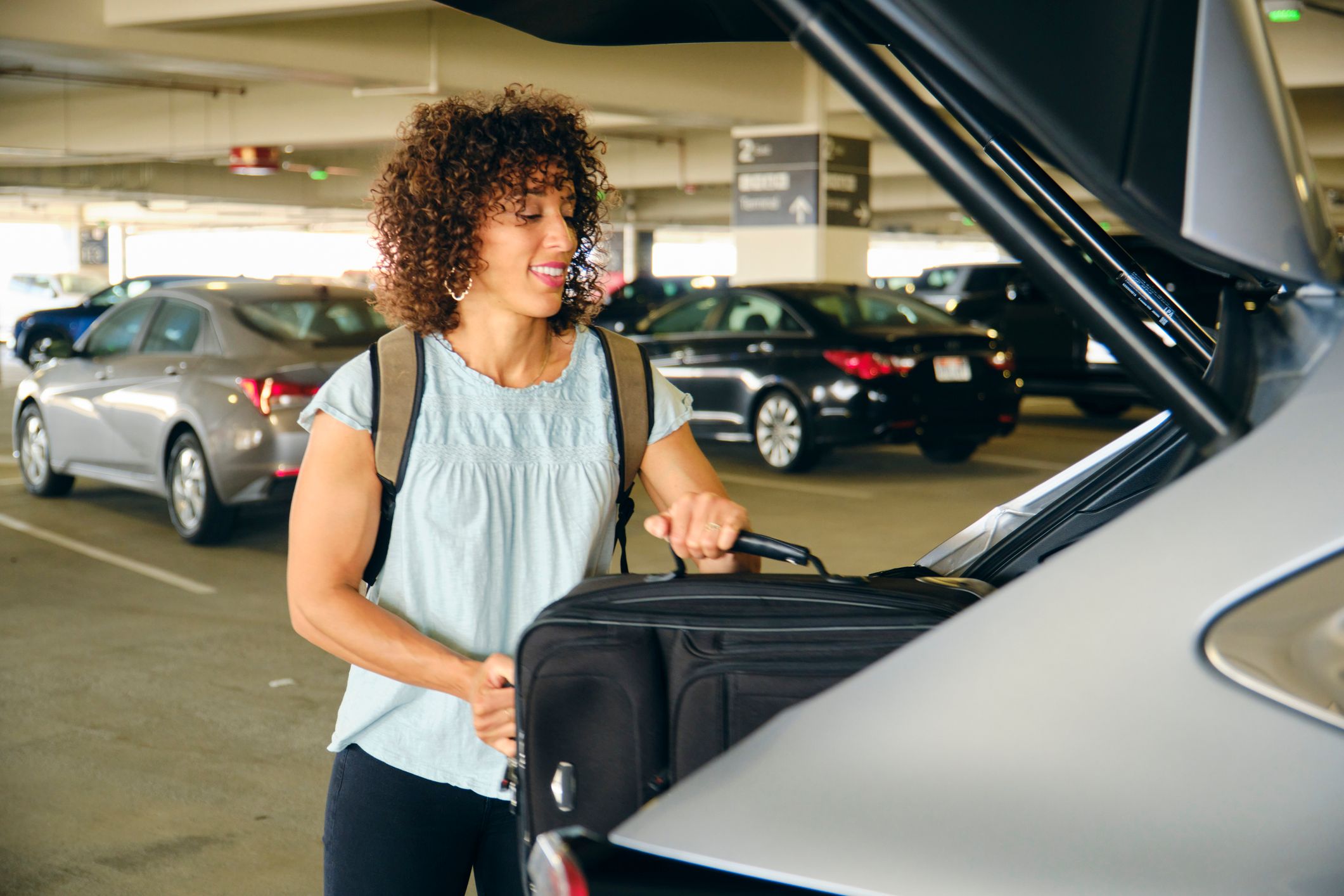 A woman getting a suitcase out of the boot of a car in an airport car park