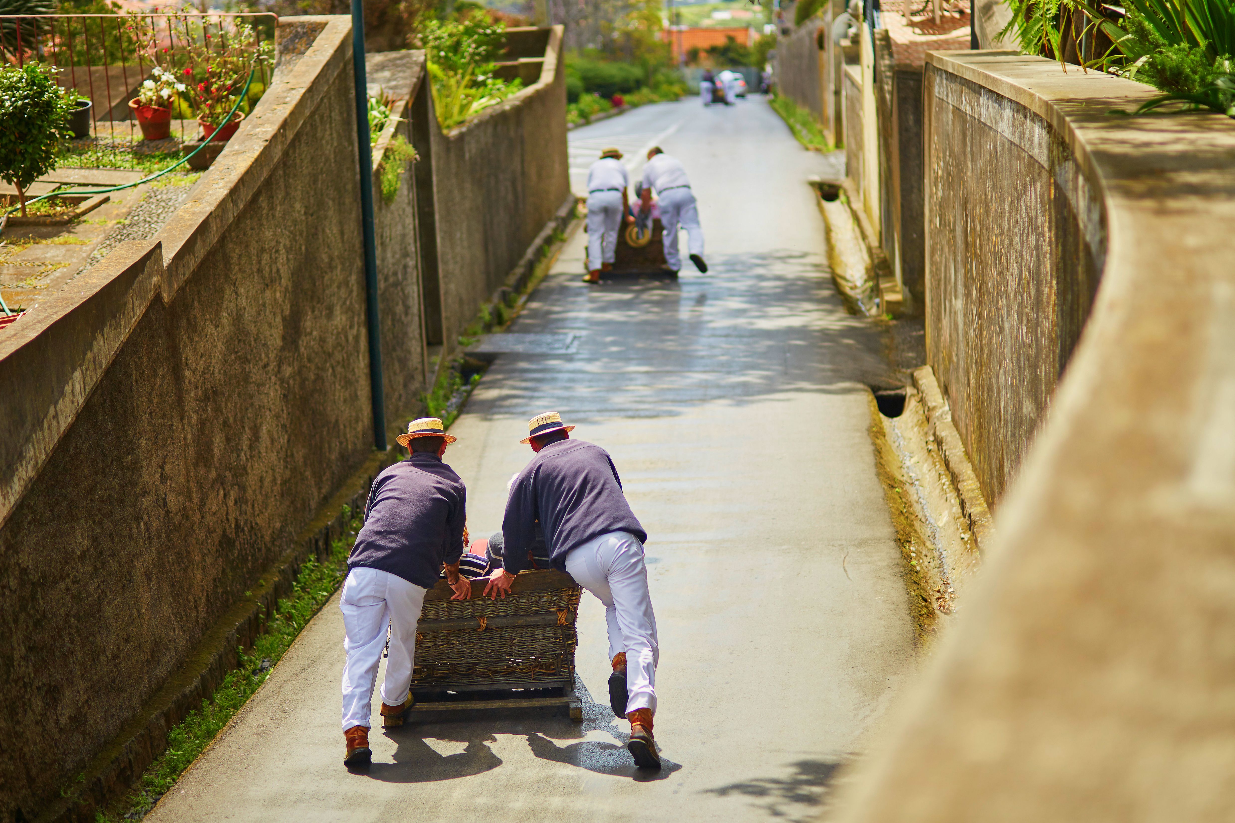 Toboggan riders pushing wooden sledge with tourists downhill - a famous tourist activity in Funchal, Madeira