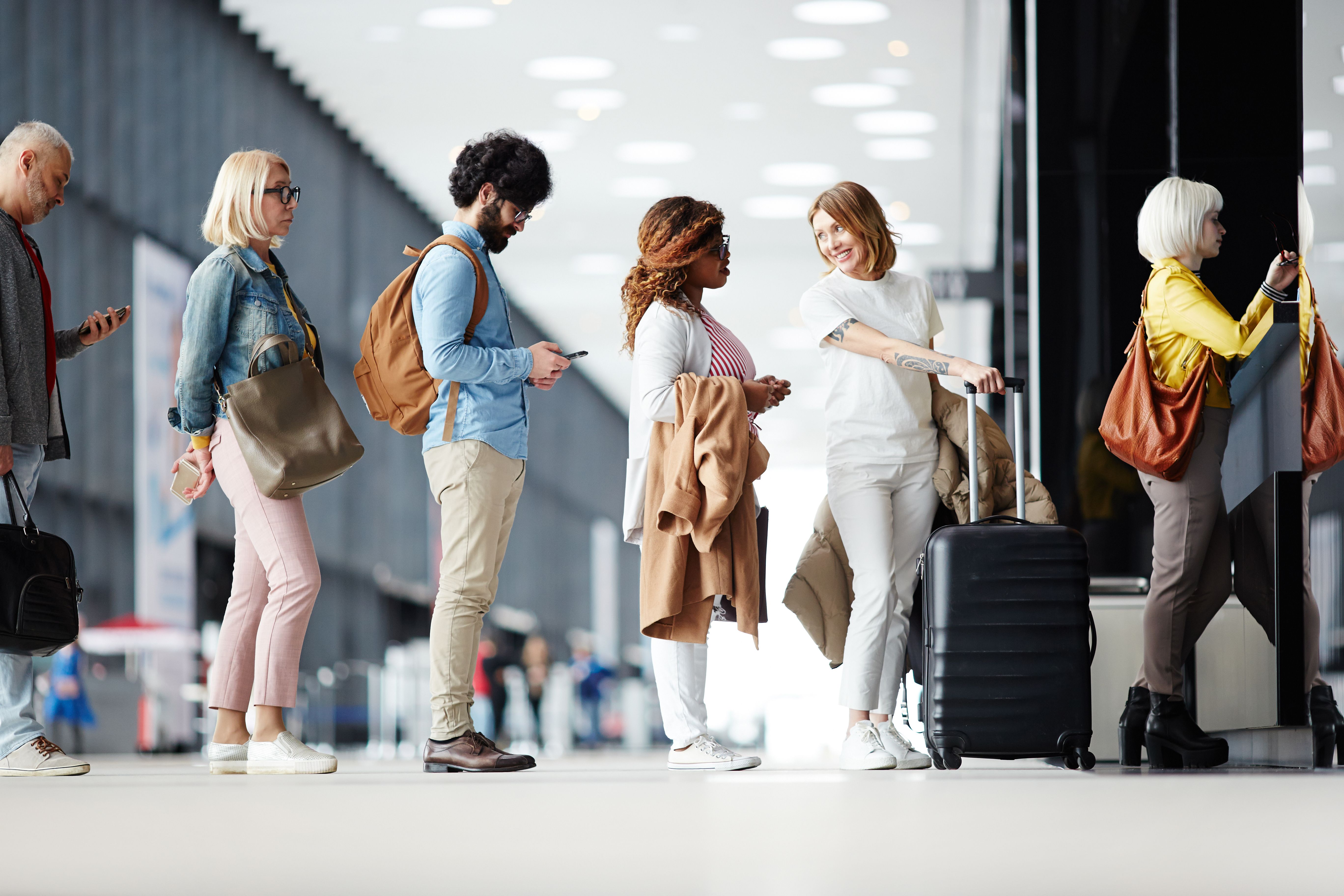 Several passengers standing in a queue while waiting for check-in registration before their flight at an airport all holding luggage