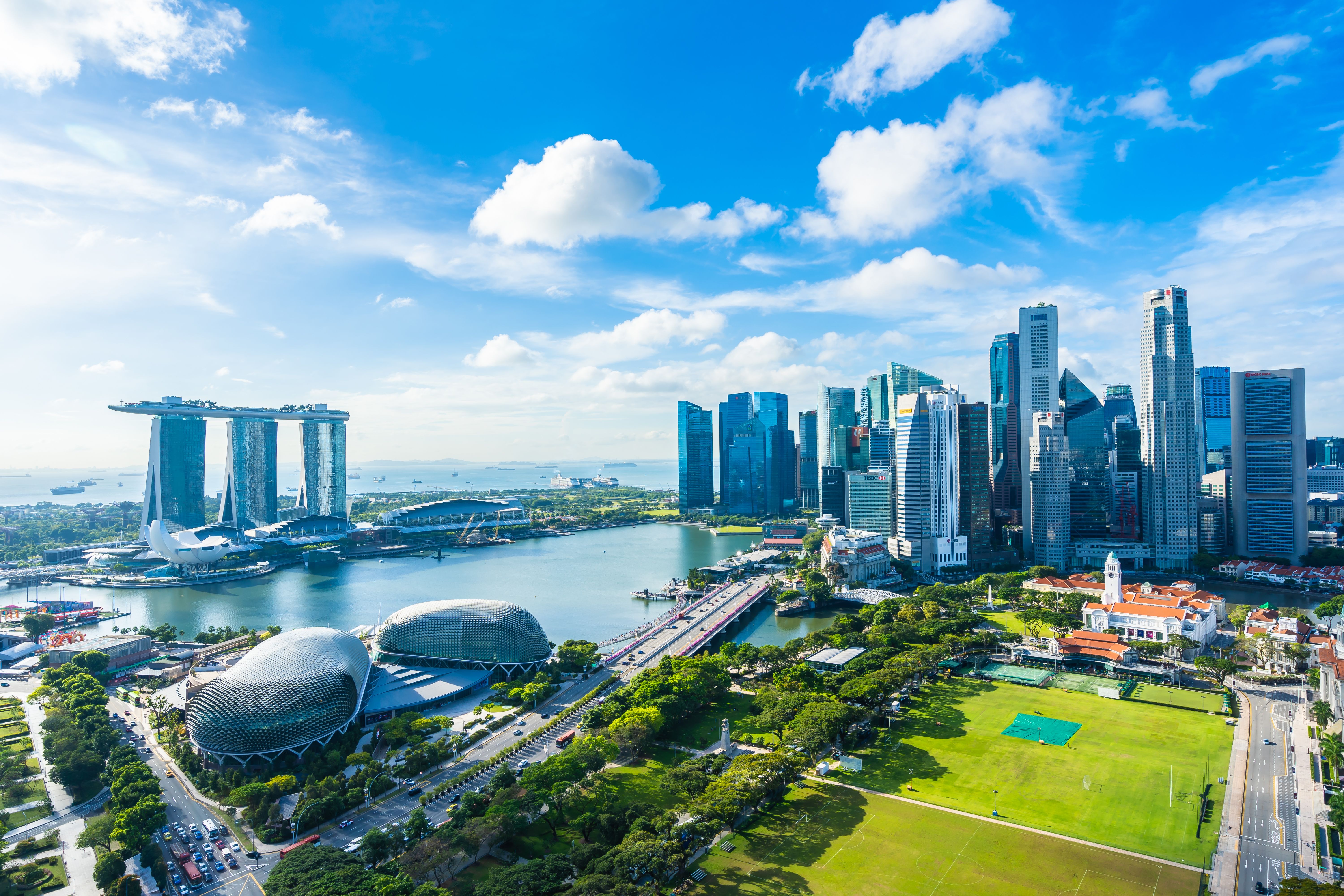 An aerial cityscape of Singapore's skyline with skyscraper buildings and a cloudy blue sky