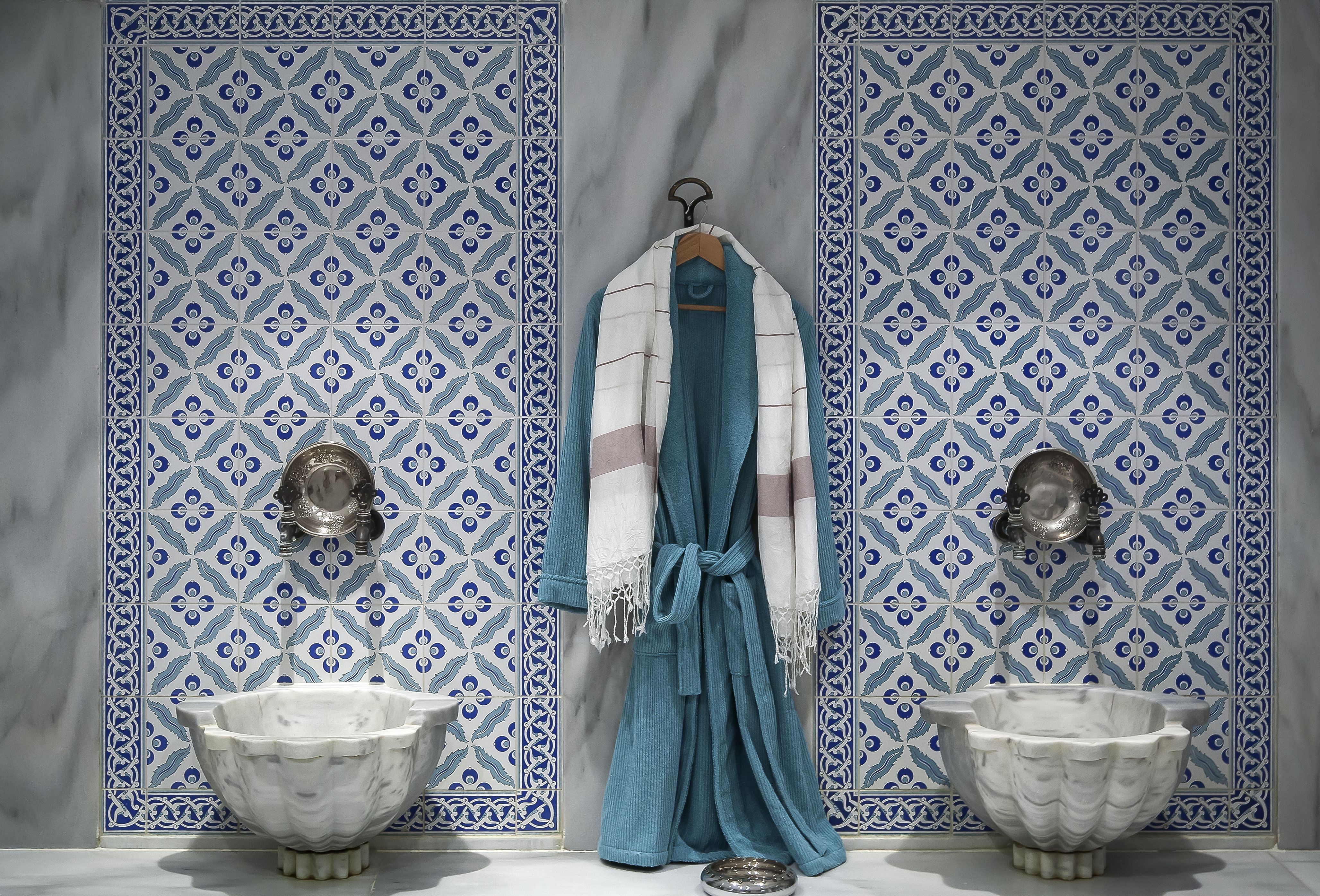 A hammam spa with mosaic walls, two sinks and a bath robe