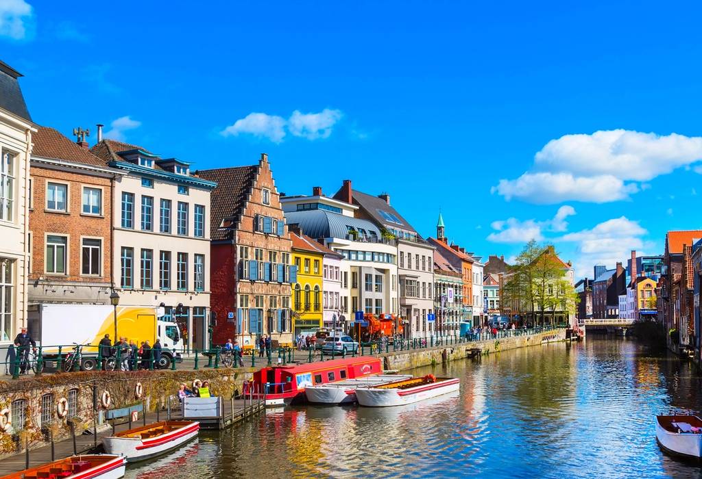 A canal side view of old colorful traditional houses and boats in Ghent, Belgium on a bright, clear day