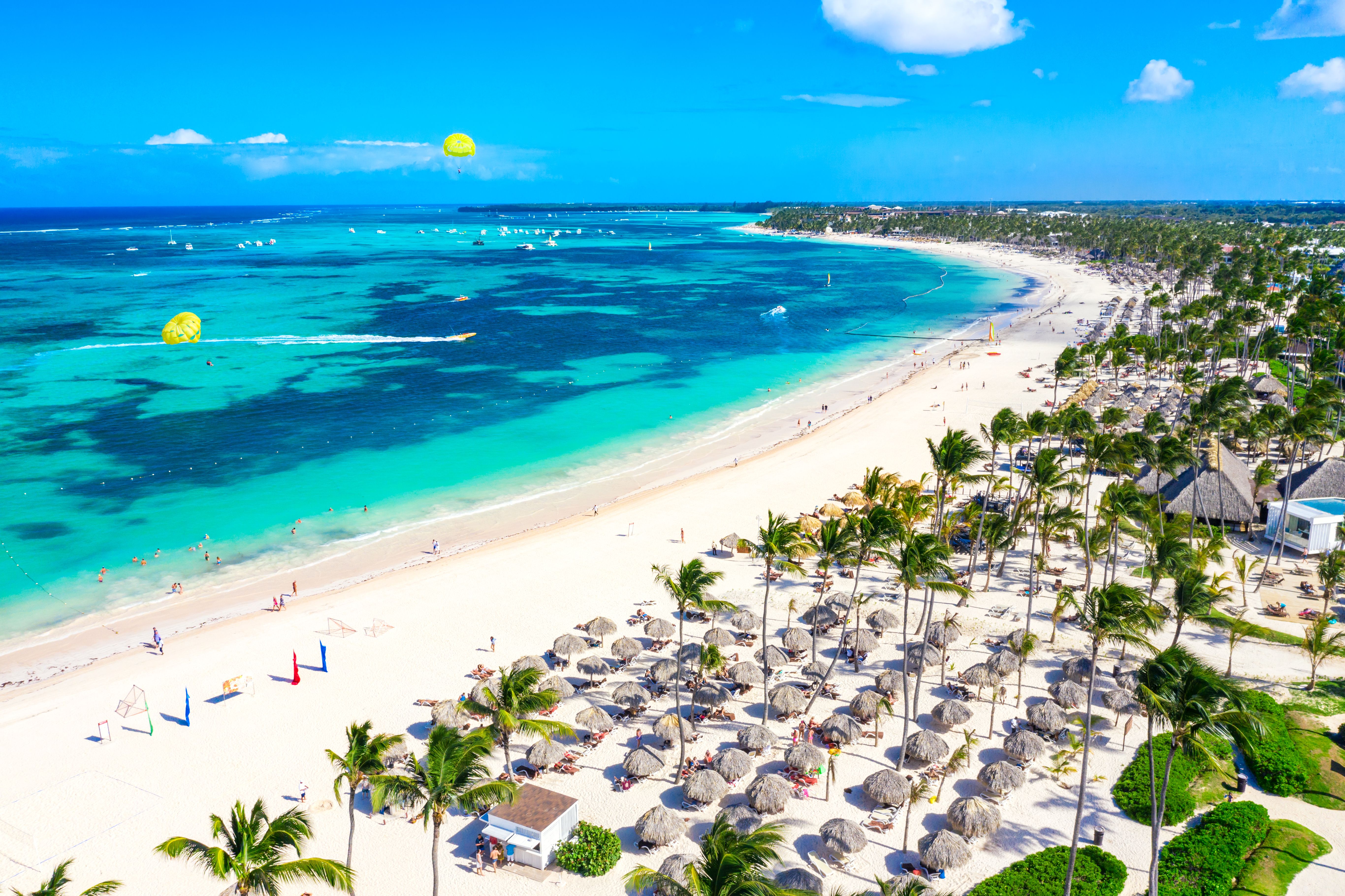 Aerial view of Bavaro beach resort in Punta Cana lined with palm trees and thatch umbrellas and with parasailing in the sea