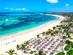 Aerial view of Bavaro beach resort in Punta Cana lined with palm trees and thatch umbrellas and with parasailing in the sea