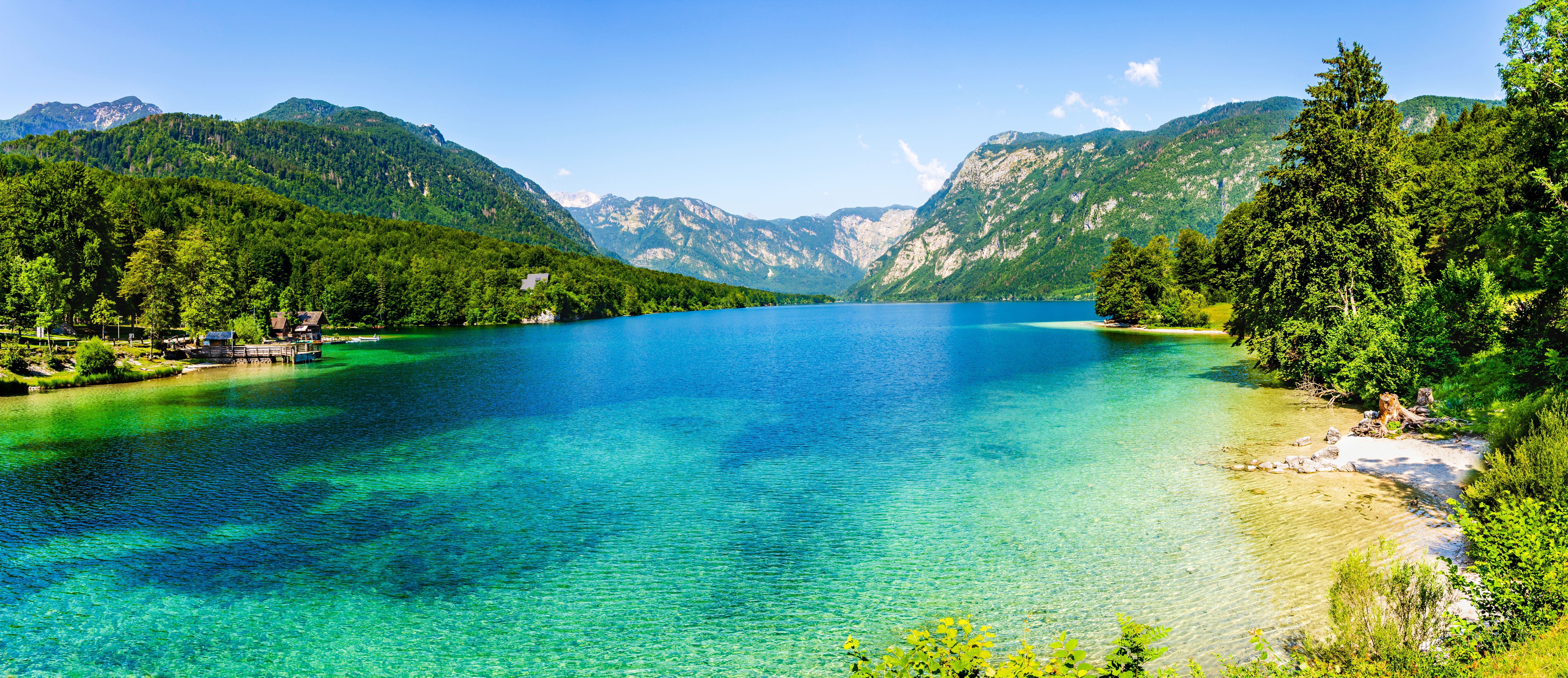 A view of the clear turquoise water of Lake Bohinj in Slovenia surrounded by verdant valley mountains