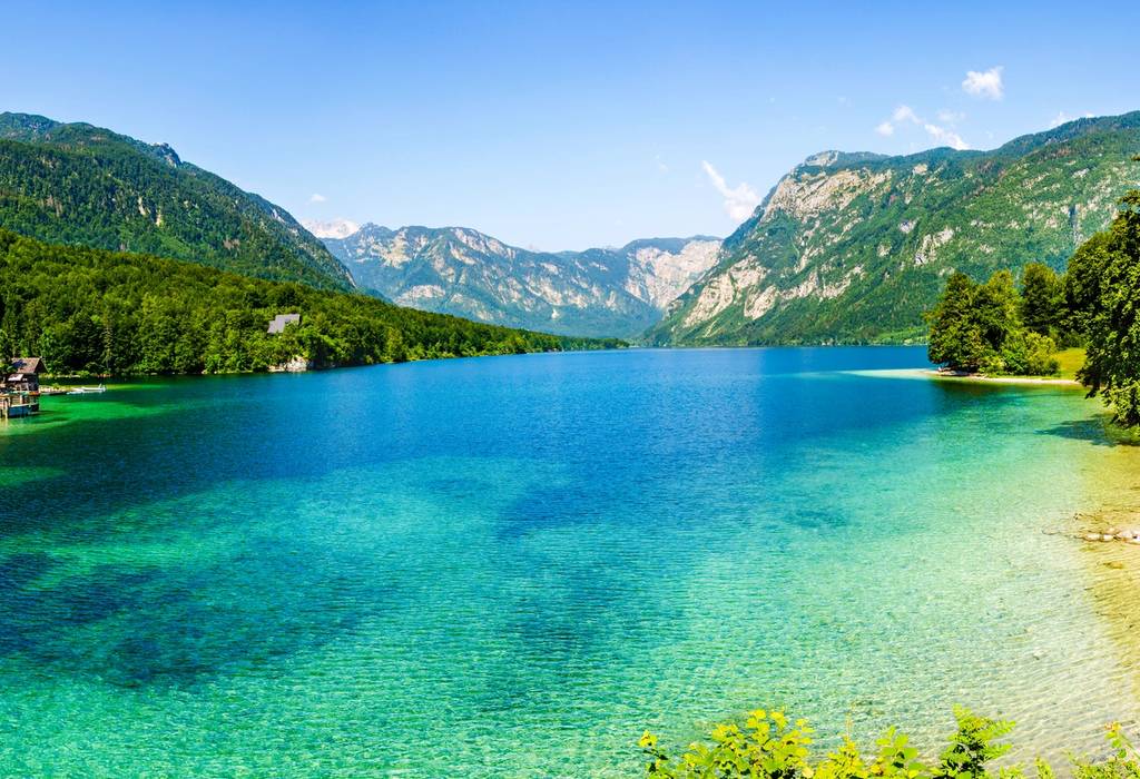 A view of the clear turquoise water of Lake Bohinj in Slovenia surrounded by verdant valley mountains