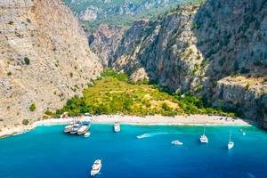 View of boats docked at Butterfly Valley Beach in Muğla, Turkey with mountains in the background