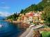 View of a small town perched on the shores of Lake Como with green trees surrounding it and boats bobbing in the water