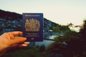 A picture of a woman holding a UK passport against the backdrop of a tropical country