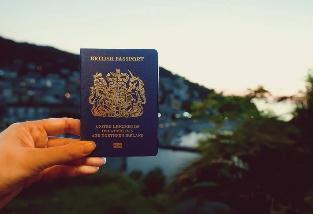 A picture of a woman holding a UK passport against the backdrop of a tropical country