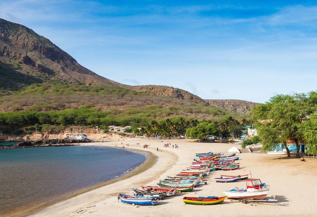 Colourful wooden fishing boats on a golden curve of sand at the foot of a mountain in Cape Verde