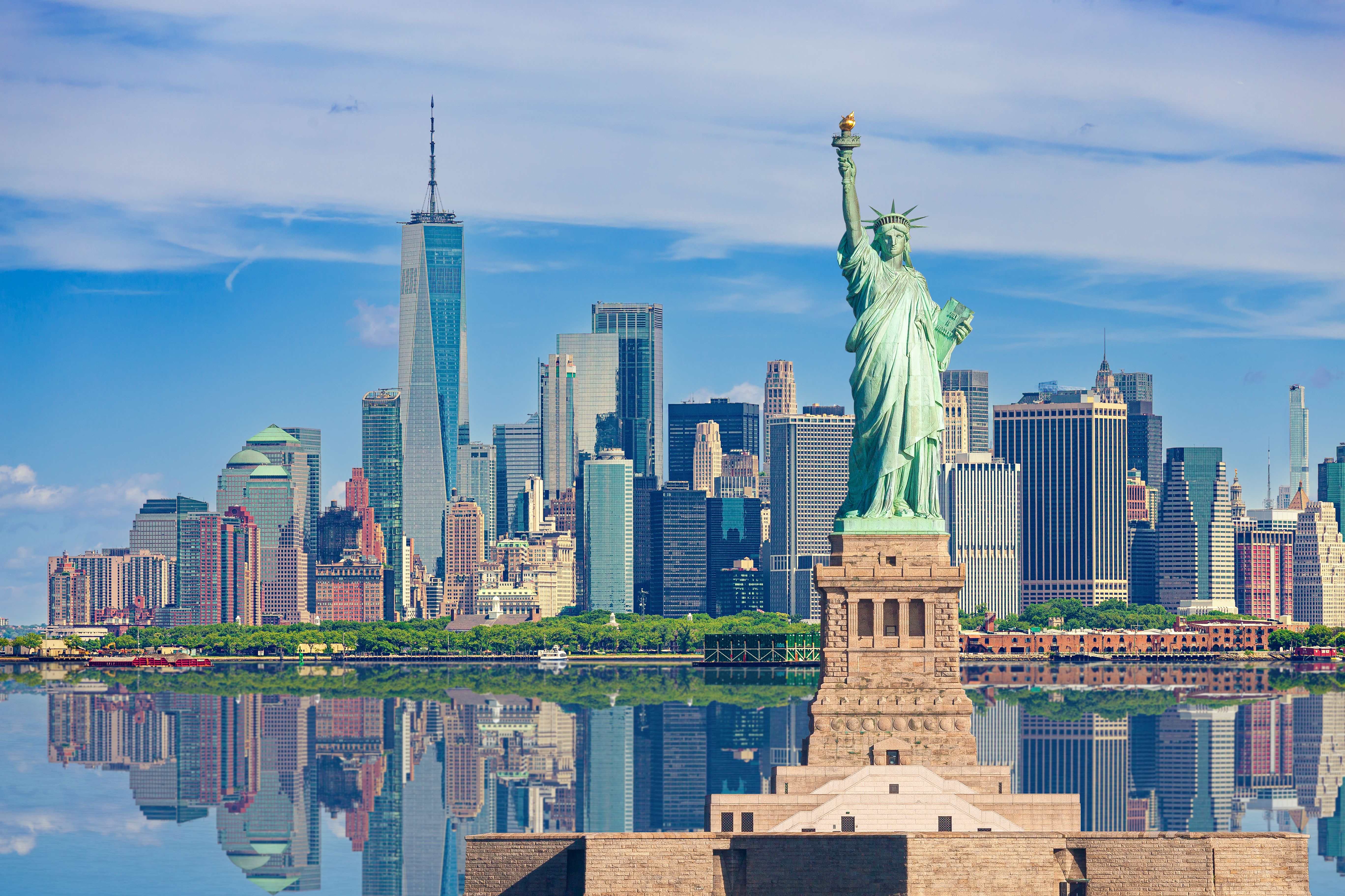 A view across the water of New York's skyline with the Statue of Liberty in the forefront and the Empire State Building in the background