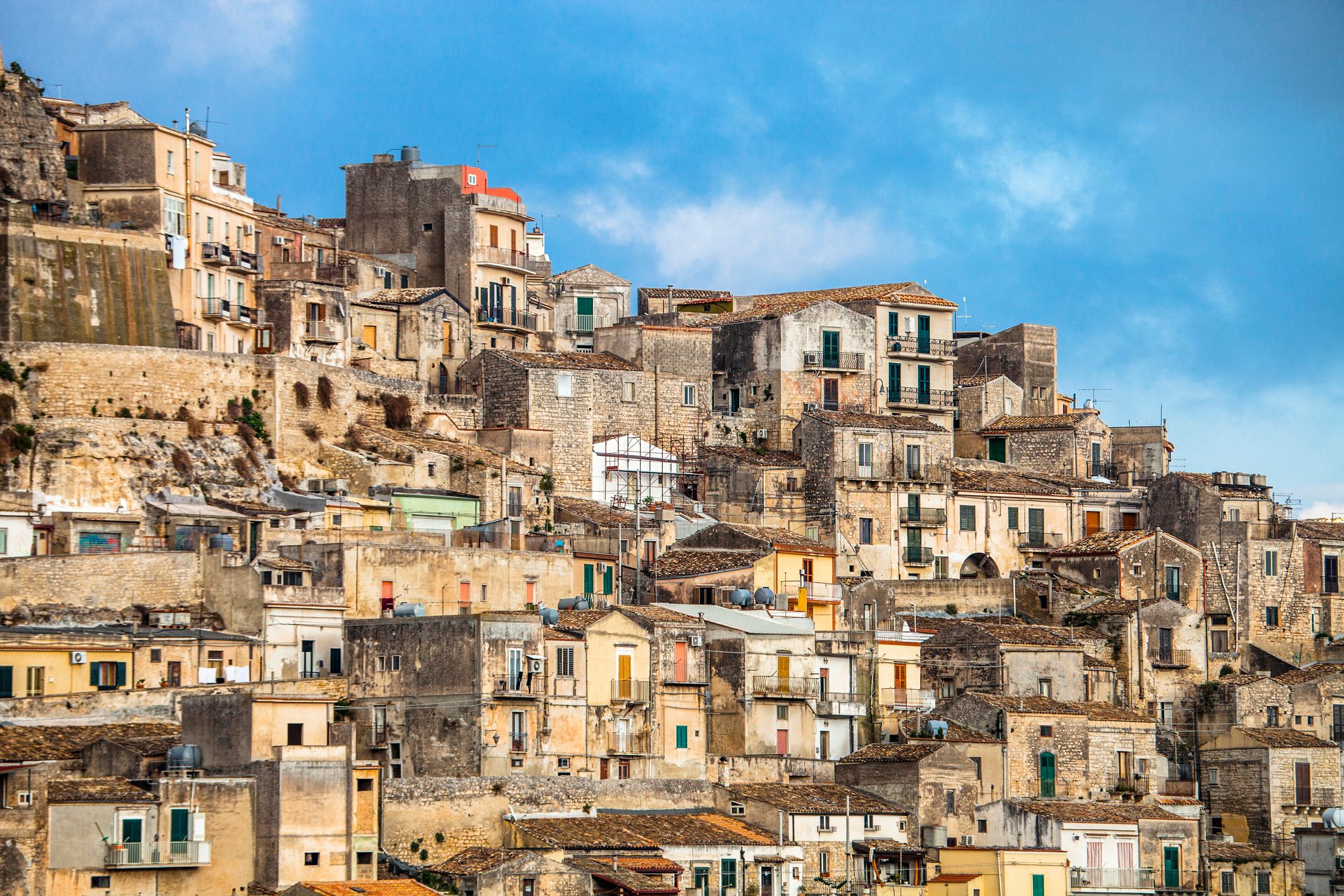View of pastel yellow and beige house squeezed side by side on a hilltop town in Sicily.