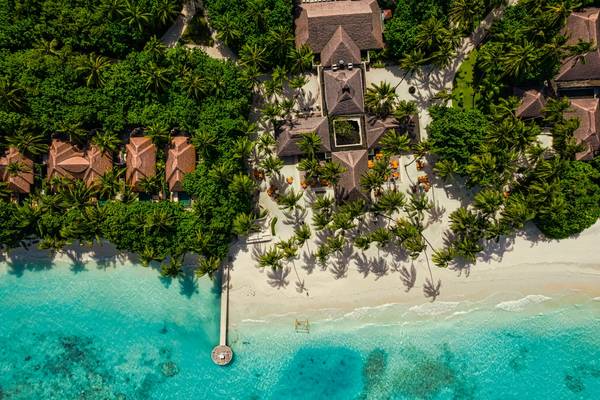 A birds-eye view of a luxury beach resort in the Maldives with a white sand beach and lots of green palm trees