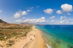 Wide view of the long stretch of golden sand on Porto Santo island with fluffy clouds in the sky and mountains in the distance