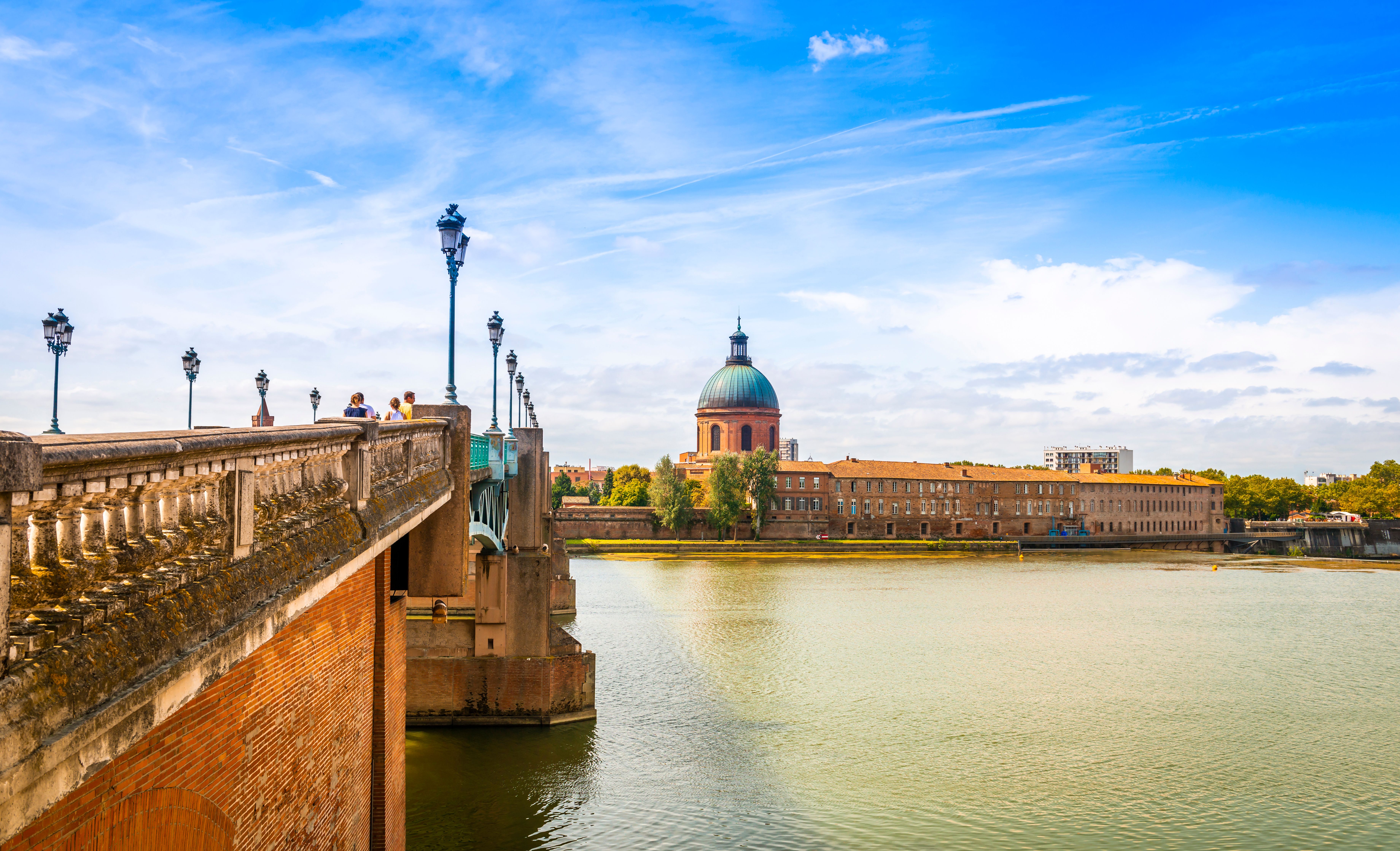 View alongside a lamp-lined bridge that stretches over a low river in France.
