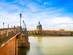 View alongside a lamp-lined bridge that stretches over a low river in France.