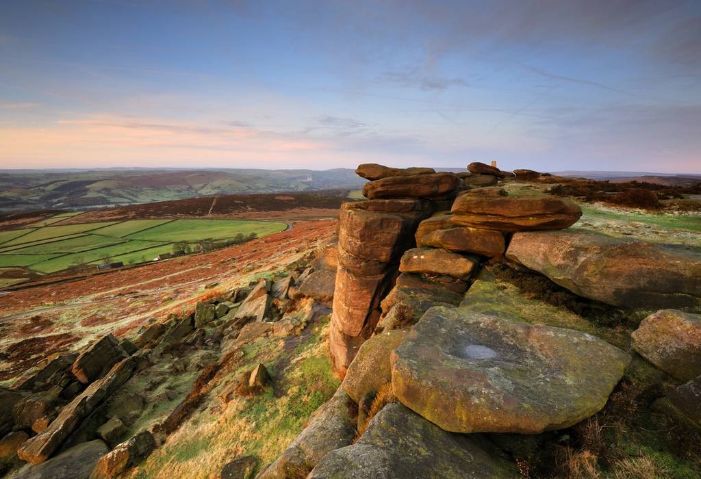 View of the rocky gritstone escarpment known as Stanage Edge looking over the green valley below
