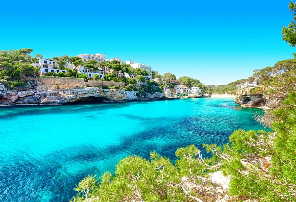 A view across a turquoise bay of Cala Santanyi beach and headland on a bright blue day in Majorca, Balearic Islands
