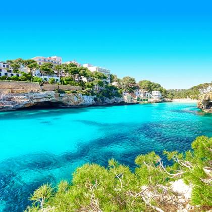 A view across a turquoise bay of Cala Santanyi beach and headland on a bright blue day in Majorca, Balearic Islands