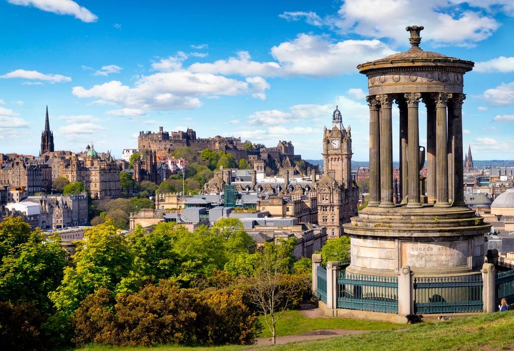 View of a columned monument and the skyline of Edinburgh, including its castle, from a Calton Hill