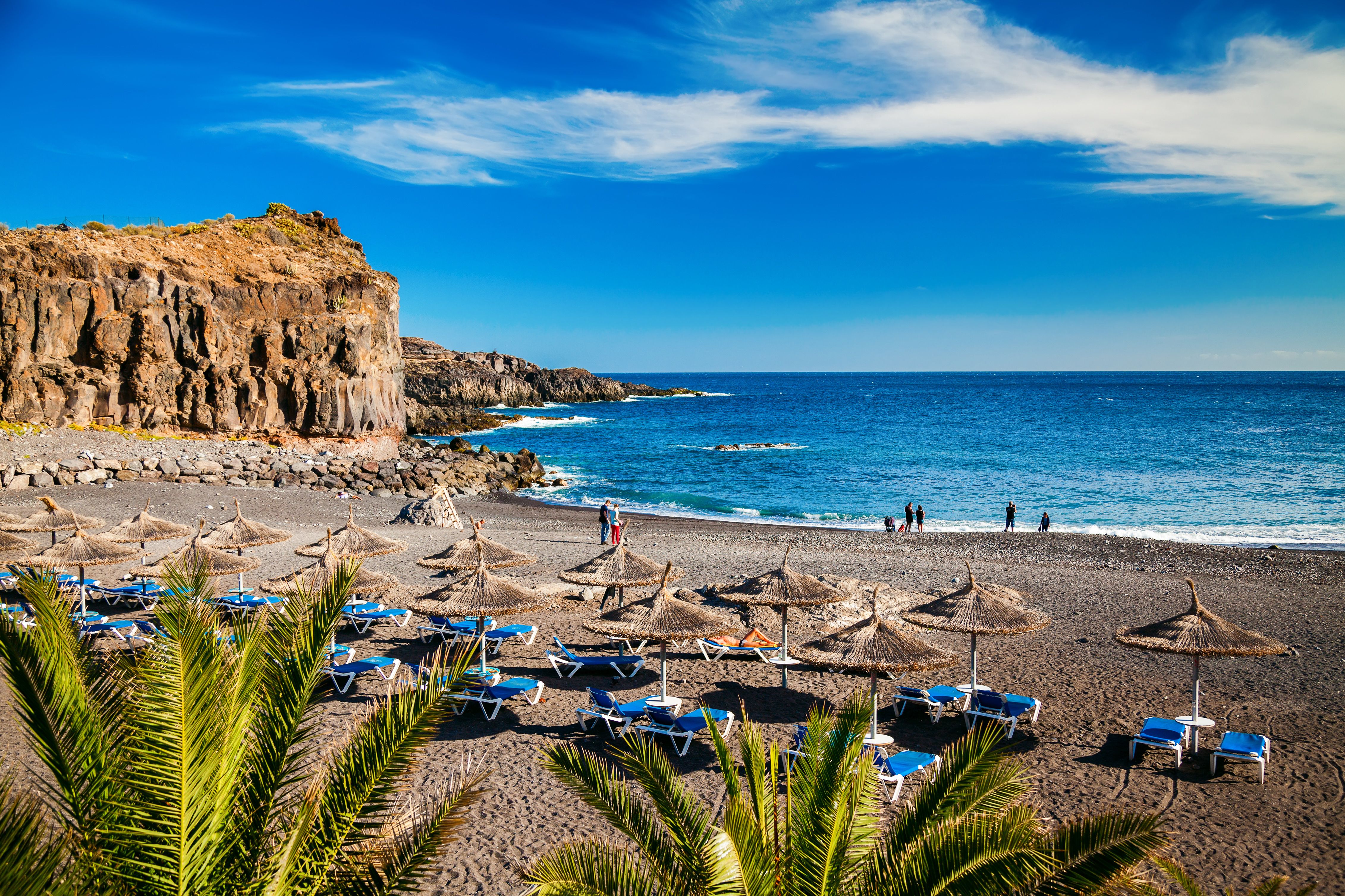 View of sun-lounger-lined volcanic sands at the small Playa de Ajabo beach in Tenerife.