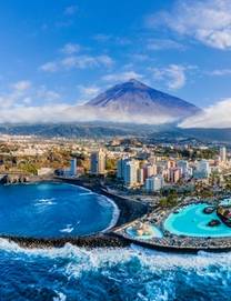 View of Mount Teide bearing over the city of Puerto de le Cruz in Tenerife, complete with a curved black-sand beach and the artifical saltwater pools of the César Manrique Maritime Park 